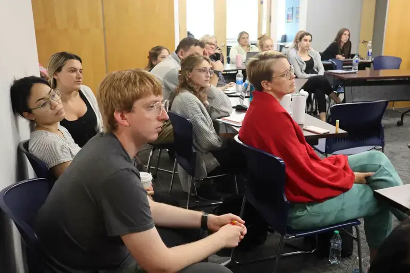 A group of students seated in chairs, engaged in a supportive counseling session in a classroom setting.