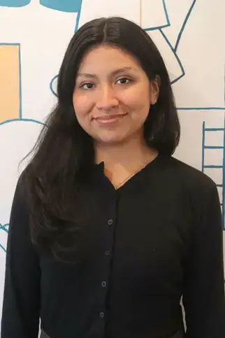 Jennifer Rojas, BS, Upper School Teaching Assistant, wearing a black shirt and brown skirt, smiling for her portrait.