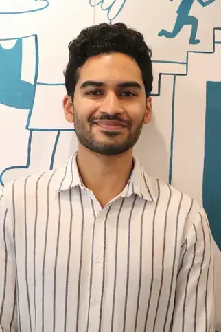 Kunal Rajesh, BFA, Upper School Lead Teacher, stands in front of a wall wearing a striped shirt.