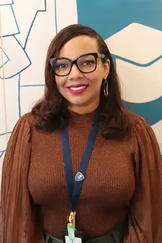 Ann Nuñez, AS, Registrar Coordinator, wearing glasses and a brown sweater, smiling for her faculty portrait.
