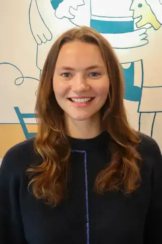 Eleanor Wefing, BA, Admissions Coordinator, smiling in a blue sweater with long hair.