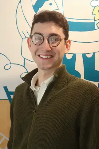 Daniel Khanan, BA, Humanities Focus Teacher, smiling in a sweater and glasses. Faculty portrait.