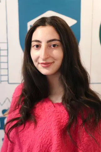 Young woman with long hair in a pink sweater, identified as Karina Shaya, Lower School Teaching Assistant.