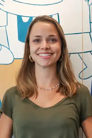 A cheerful woman stands before a bright, colorful wall, radiating positivity and warmth in her faculty portrait.